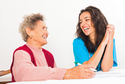 Happy elderly lady laughing with kind nurse carer working in homecare.