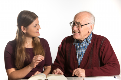young woman helping senior man to pronounce sound and read book, man has dementia